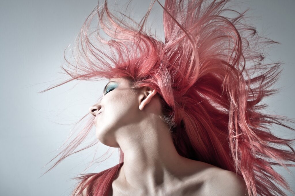 Image of a girl with blue eye makeup flipping her pink colored hair
