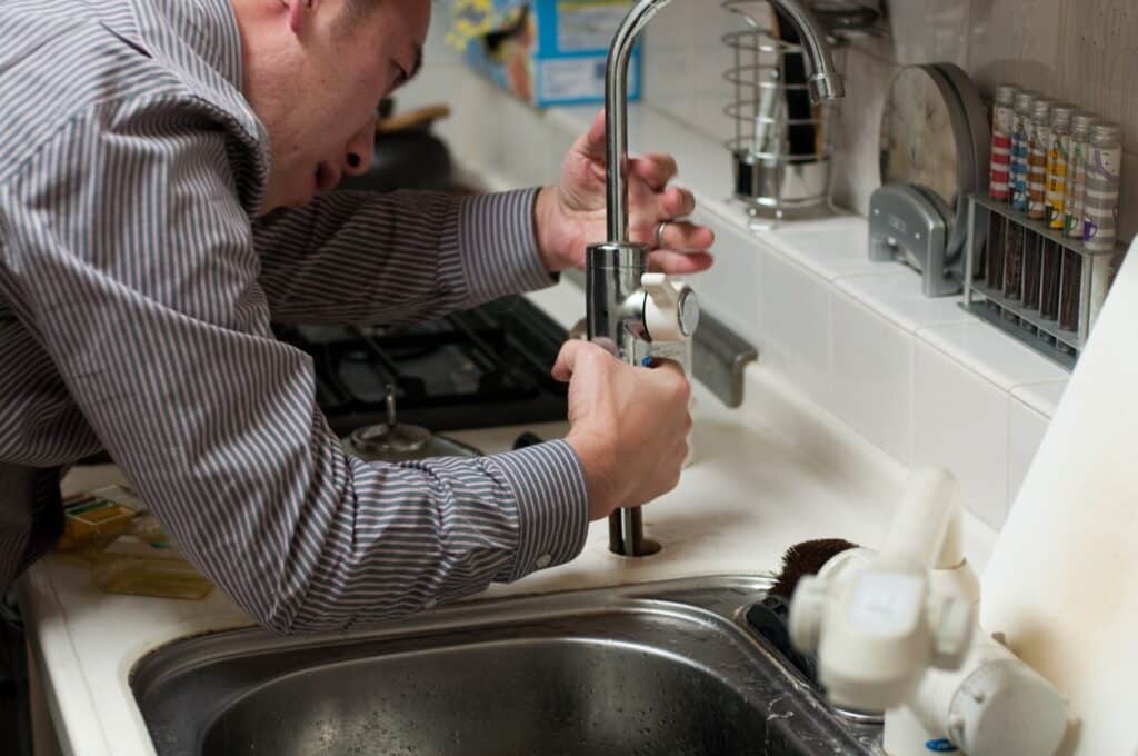 Image of a plumber fixing a kitchen faucet